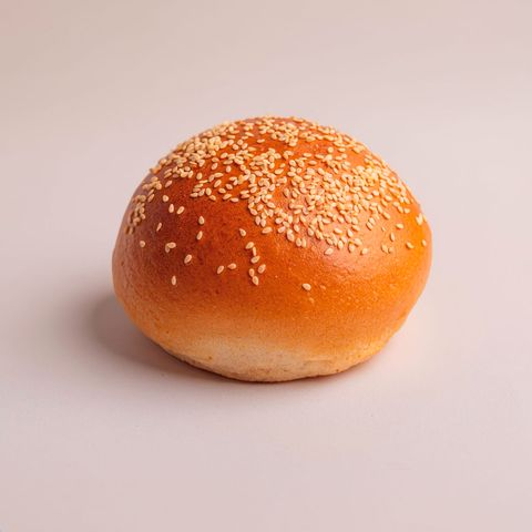 A soft, domed white-sesame burger bun seen from the side